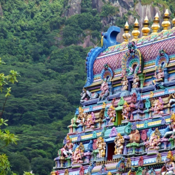 Farverig gopuram på et hindu‑tempel i Sydindien med detaljerede skulpturer af guder og mytologiske figurer – omgivet af frodig grøn natur, der fremhæver den spirituelle og kunstneriske rigdom i indisk kultur.